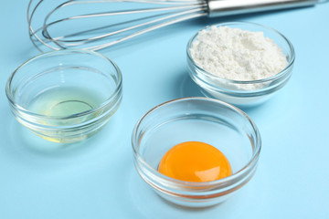 Egg yolk, white and flour in bowls on light blue background, closeup