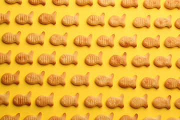 Delicious goldfish crackers on yellow background, flat lay