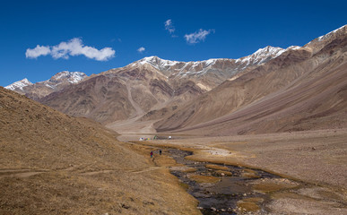 Two persons walk towards Chandra Tal on a clear day.