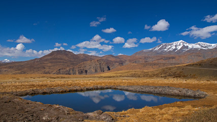 Water reserve on barren land of Spiti Valley - Blue sky with white clouds and reflection.