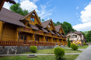 Modern wooden houses from a felling on a background of mountains. Wooden houses with landscaped area on a background of mountains. Traditional wooden cottages at sunny day. 