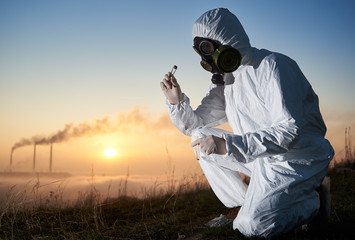 Crouched researcher working outdoors on the hill collecting samples for his study, smoking stacks...