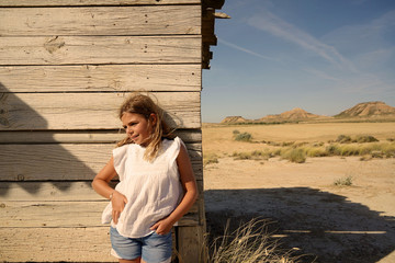 Young blond girl standing by woodhouse in the Bardenas Reales National Park