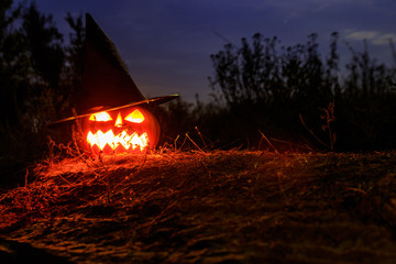 Spooky Halloween pumpkin jack-o-lantern in witch hat with burning candles in scary forest at night