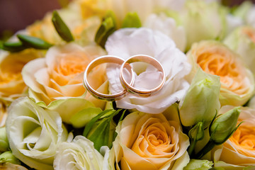 Wedding rings lie on a bouquet of beige roses
