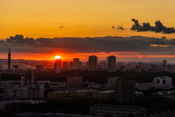 Black silhouettes of buildings are on a red sky background with orange and yellow sunset