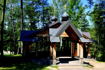 Fototapeta na wymiar A view of a small Orthodox shrine with a slanted decorated roof and wooden beams as supports standing in the middle of a dense forest or moor seen on a sunny summer day in Poland