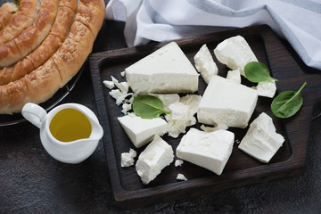 Black wooden serving board with blocks of feta cheese, olive oil and spanakopita pie, studio shot,...