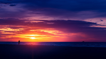 Fototapeta na wymiar Silhouette of man taking photos of dramatic cloudscape at sunrise over ocean