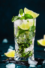 Mojito cocktail or mocktail with lime, mint, and ice in glass on blue background. Summer cold alcoholic non-alcoholic drink,  beverage and cocktail. Copy space
