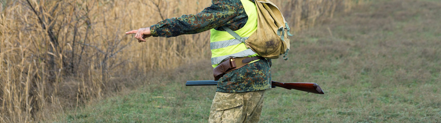Silhouette of a hunter with a gun in the reeds against the sun, an ambush for ducks with dogs