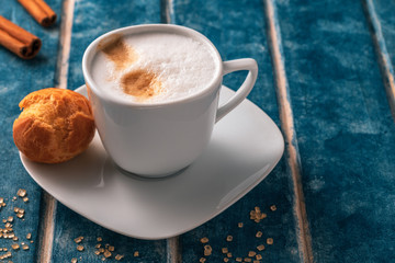 Cup of cappuccino, eclair, strawberries and cinnamon sticks on a background of blue wooden boards.