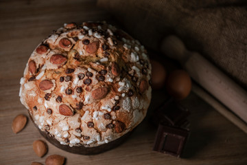 Panettone, typical Italian Christmas cake with chocolate and almonds. In the background the ingredients used to make panettone, eggs, flour, chocolate.
