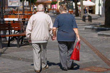 Senior couple holding hands in gloves and walking on city street during coronavirus spreading. Romantic senior couple holding hands while walking together to protect each other from virus infection