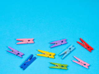 Colored clothespins or clothes peg collection on blue background and free space for text. Set of wooden colorful yellow, green, red, blue and pink item. Different bright colors and positions