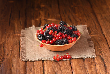 Blackberries and red currants in a wooden plate.