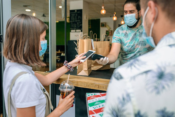 Young woman with mask paying with mobile a take away order