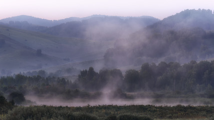 landscape in the early morning with fog over the water, mountains in the background