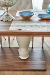 Wooden dinner table on massive legs with dishware in modern apartment. Close-up