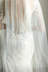 Back of white bride in white wedding dress with veil standing in the room. Back view. Soft focus