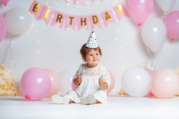 little girl in a cap dress sits in the background with garlands and balloons