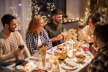 holidays, celebration and people concept - happy friends having christmas dinner at home drinking...