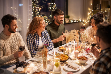 holidays, celebration and people concept - happy friends having christmas dinner at home drinking non-alcoholic red wine