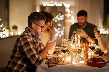 holidays and people concept - man with smartphone at dinner party with friends at home
