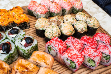 Different types of delicious and juicy sushi and rolls on a wooden board