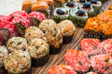 Different types of delicious and juicy sushi and rolls on a wooden board