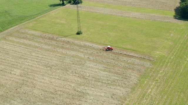 Aerial view of red tractor with tedders, drying mowed hay