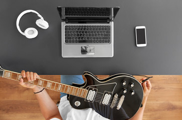 leisure, music and people concept - young man or musician with laptop computer tuning guitar sitting at table