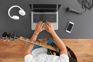 leisure, music and people concept - young man or musician with laptop computer and guitar sitting at table - 374085956