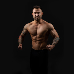Fototapeta na wymiar Handsome bodybuilder man with an ideal body, after coaching abdominal muscles, biceps, triceps on dark background.