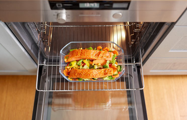 food, eating and culinary concept - salmon fish with vegetables cooking in baking dish in oven at...