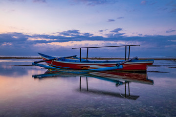 Seascape. Fisherman boat jukung. Traditional fishing boat at the beach during sunset. Cloudy sky. Amazing water reflection. Thomas beach, Bali