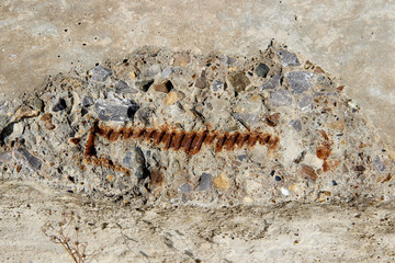 A partially seen rusty reinforcement rod in a damaged reinforced concrete slab