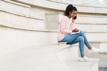 Image of african american girl talking on cellphone while sitting