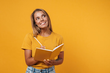 Image of young happy woman thinking and writing in exercise book