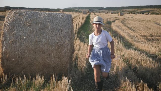 Little girl in a field with haystack run at sunset in the countryside.