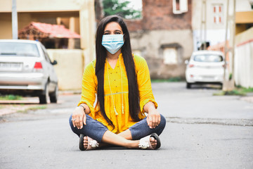 Portrait of Indian girl in mask sitting on street and staring at camera.