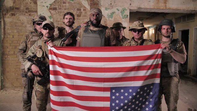 Squad of diverse US army men in camouflage holding flag upside down expressing disagreement with country's foreign policy. Multi-ethnic military males transmitting distress signal using US flag