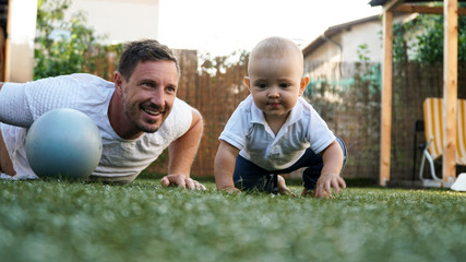 A cute baby and his smiling father playing on a grass with a pilates ball