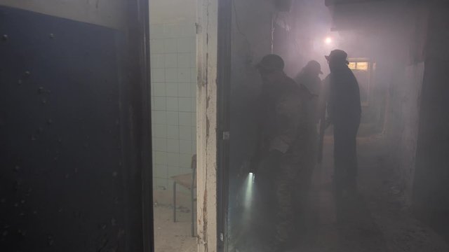 Three experienced special forces fighters throwing granade and opening fire through doorway while suspecting presence of enemy in a room of captured ruined building. Well-coordinated trio on mission