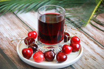 Burgundy drink in a glass and a natural cherry on a plate