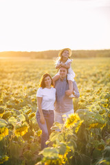Happy family is playing, having fun on the field with sunflowers at sunset.