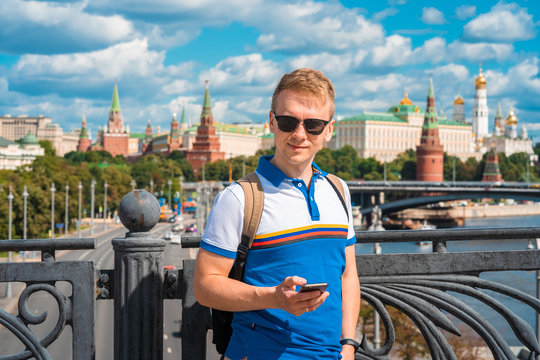A young blond man calls on a mobile phone with a view of the Kremlin and the river in Moscow