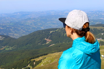 Fototapeta na wymiar A girl admires the view from the summit of Mount Cimone at 2,165 meters above sea level on the Modenese Apennines