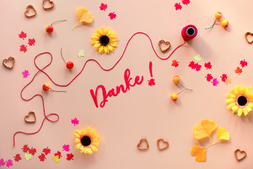 Obraz premium Danke means Thank you in German language. Fall decorations - yellow flowers, orange gingko leaves, maple leaf paper confetti, heart shape pretzel snacks. Autumn flat lay on orange background.
