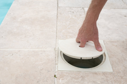Hand removing the lid from a swimming pool skimmer